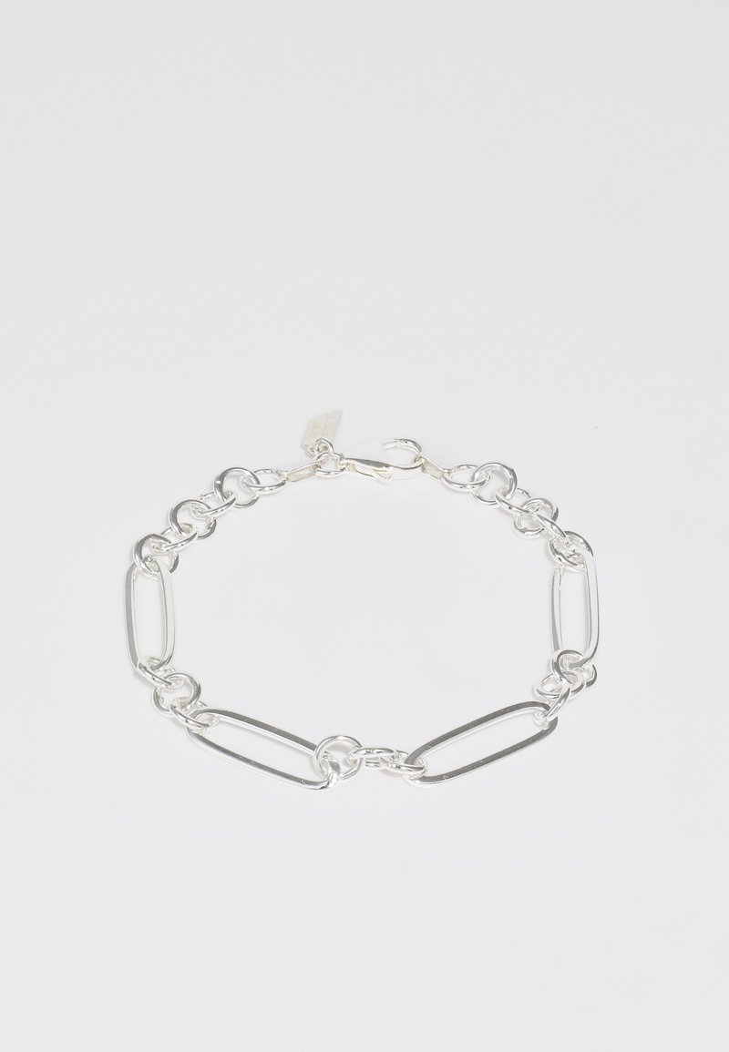 Silverfärgad kedjebracelet med avlånga ovala länkar och rundade detaljer, med ett lås för fäste. Slät, polerad yta.