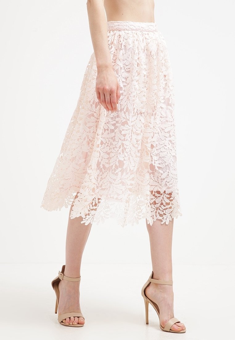 Falda midi de encaje en rosa claro, con un patrón floral, cintura elástica y dobladillo en forma de pico, combinada con sandalias de tacón nude.