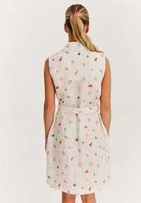 Jasno-beżowa sukienka bez rękawów z kolorowymi haftowanymi wzorami, kołnierzykiem, bocznymi kieszeniami oraz paskiem podkreślającym talię.