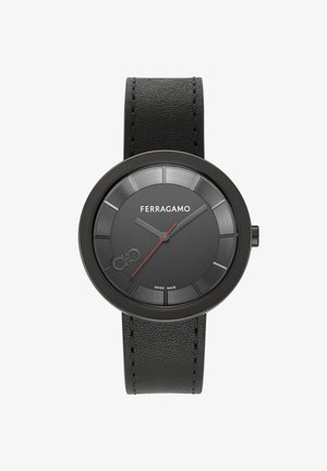 Reloj con correa de cuero negro, caja redonda de color negro mate, esfera negra texturizada y manecilla de la hora roja en contraste. Presenta una artesanía suiza.