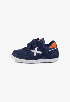 Chaussure pour enfants bleu marine en daim et tissu, avec un motif croisé blanc, deux bandes Velcro, et une semelle en caoutchouc texturé blanc.