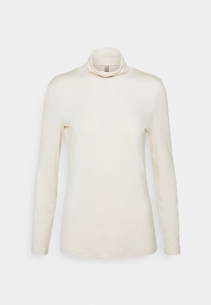 Long-sleeve, cream turtleneck top made from smooth, stretchy fabric. Features a soft cowl neck and fitted silhouette. No patterns or embellishments.