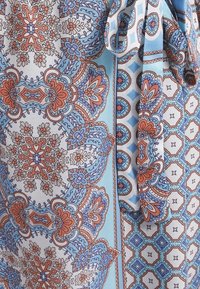 Tissu bleu, orange et blanc avec des motifs géométriques et floraux complexes, présentant un détail de ceinture nouée sur un matériau doux et fluide.
