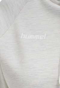 Felpa grigia chiara con un tessuto testurizzato. Presenta un logo impresso bianco "hummel". Il design include maniche raglan e un collo pulito.