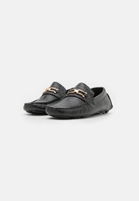 Mocassins en cuir noir avec une finition texturée, dotées d'un accent en métal doré. Bout rond et design de semelle flexible.