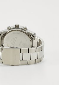 Reloj de acero inoxidable con una pulsera pulida, una caja redonda, múltiples botones de corona y un fondo de caja grabado. Color predominantemente plateado.