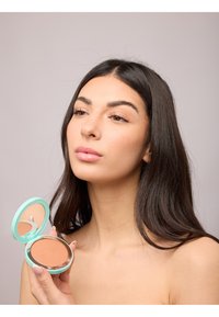 Kompakter Bronzer mit einem mintgrünen Gehäuse und einem spiegelnden Deckel, der ein glattes, hellbraunes Puder zeigt. Die Textur erscheint matt.