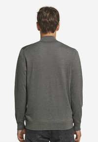 Mörkgrå stickad tröja med hög krage, långa ärmar och en slät yta, med ribbade muddar och fåll.