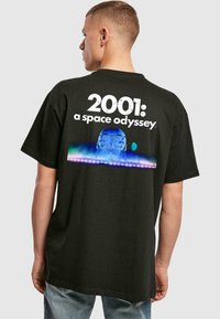 Svart bomull t-skjorte med "2001: En romodyssé" grafikk i hvit tekst og fargerik rom-motiv på baksiden. Avslappet passform.