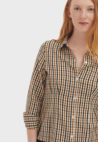 Brown and cream checkered button-up shirt with a collar, roll-up sleeves, and white buttons. Soft fabric with a structured fit.