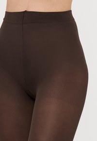 Hnědé legíny z pružného materiálu s hladkou texturou, vybavené širokým elastickým páskem a přiléhavým střihem.