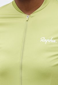 Κοντινό πλάνο ελαφρώς πράσινου ποδηλατικού τζέρσεϊ με μπροστινό φερμουάρ και λευκό λογότυπο "Rapha" στο αριστερό στήθος.