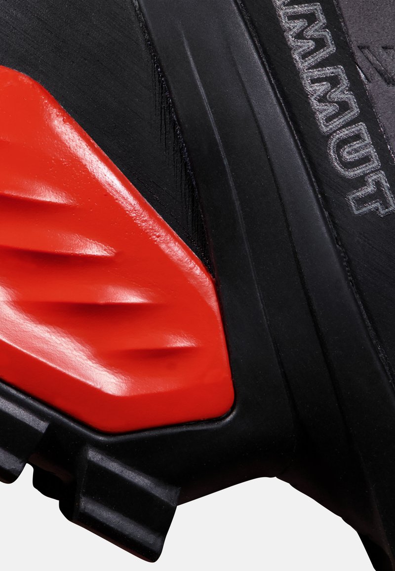 Scarpa da trekking nera con un accento rosso texturizzato, caratterizzata da motivi scanalati e una suola in gomma robusta. Logo del marchio visibile.