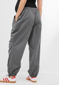 Jogging gris léger avec taille élastique, poches latérales et poignets élastiques, assorti à des chaussures blanches avec des accents rouges.