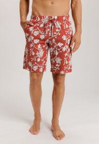 Rote Badeshorts mit einem weißen Blumenmuster, elastischem Bund und Kordelzug. Hergestellt aus leichtem Stoff, knielange Ausführung.