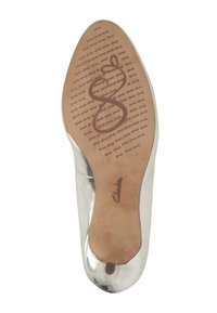 Zapato plano metálico plateado con puntera redondeada y un interior suave. La suela presenta un patrón texturizado con la marca, proporcionando agarre.