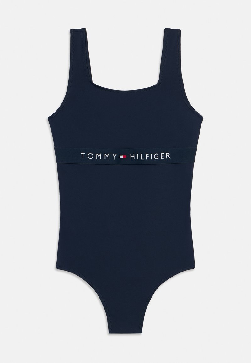 Μαγιό σε ναυτικό μπλε με τετράγωνη λαιμόκοψη και φαρδιές τιράντες, με μια αντίθετη λευκή ταινία με το λογότυπο "TOMMY HILFIGER" γύρω από τη μέση.