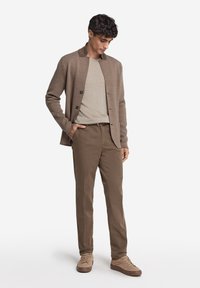 Brauner Cardigan mit Knopfverschluss, beiges T-Shirt, braune Hose und hellbraune Sneaker. Die Stoffe wirken weich; das Design ist l�ässig und figurbetont.