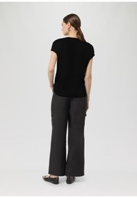 Black short-sleeve top with a relaxed fit, paired with loose-fitting charcoal trousers featuring cargo pockets and flat black shoes.