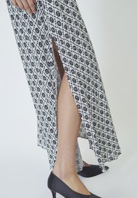Rochie lungă cu imprimeu floral alb-negru, cu slituri laterale, asortată cu pantofi cu toc înalt negri. Textură fină a țesăturii.