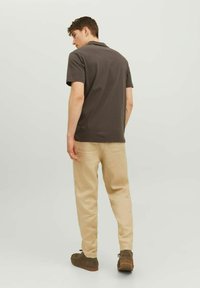 La maglietta polo grigia presenta maniche corte e colletto; abbinata a pantaloni beige chiaro e scarpe marroni scure. Design semplice, senza motivi.