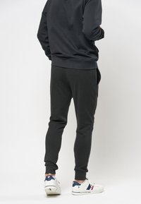 Svarta sweatpants med en tapered passform, sidofickor, elastisk midja och avslutade anklar. I kombination med vita sneakers med färgaccenter.