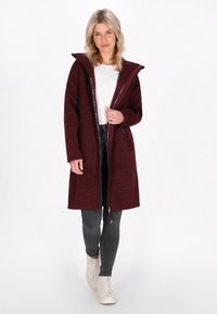 Burgundy hosszú kabát kapucnival, texturált szövetből készült. Oldalsó zsebekkel és cipzáras elülső részel rendelkezik, mintás béléssel.