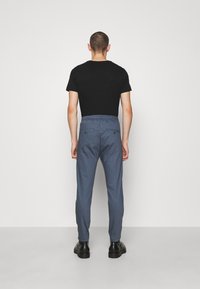 Ljusblå tapered byxor med elastisk midja, två bakfickor och en slät textur, i kombination med en svart kortärmad skjorta.