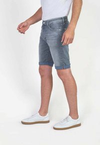 Denim shorts in vervaagd blauw met opgerolde boorden, voorzien van een klassieke vijf-pocketontwerp en knoopsluiting. Gepaard met witte sneakers.