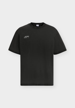 Μαύρο t-shirt με κοντά μανίκια και στρογγυλή λαιμόκοψη με μικρό λευκό λογότυπο ARKK στο πάνω αριστερό μέρος του στήθους, με φόντο απλό και ανοιχτό.