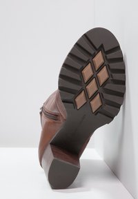 Botte en cuir marron avec un tige texturée, fermeture éclair latérale et une semelle en caoutchouc noir robuste dotée d'un motif de crampons prononcé et d'un talon en bois.