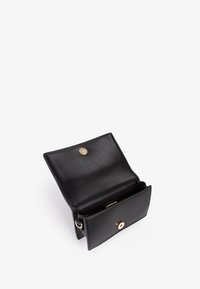 Cartera de cuero negro con una textura suave, cierre a presión y un único compartimento. Presenta costuras sutiles y un acento metálico.