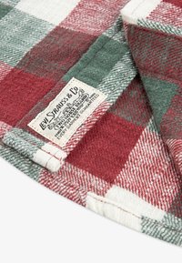 Geruite flanellen stof in rood, groen en wit. Bevat een genaaide label met "Levi Strauss & Co.", een zachte textuur en een gevouwen rand.