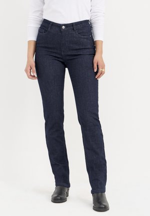 Dunkelblaue Jeans aus Denim mit schmalem Bund, geradem Bein, Fronttaschen und dezenten Nahtdetails; kombiniert mit schwarzen Knöchel-Stiefeln.