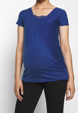 Graviditetsbluse i dyb blå med v-udskæring, korte ærmer, rynkning i siden og et blonderelief ved halsudskæringen. Blødt materiale.