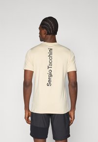 Ανοιχτό καφέ κοντό μανίκι μπλουζάκι με λαιμόκοψη τύπου crew, που διαθέτει κάθετη εκτύπωση μαύρου λογότυπου στην πλάτη. Λείος ιστός και κομψή εφαρμογή.