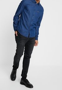 Blå denimskjorta med knappar och bröstficka, kombinerad med svarta rakpassformade jeans och svarta läderkängor.