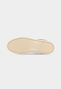 Semelle extérieure de chaussure avec une semelle en caoutchouc beige, un motif de grip texturé et le logo "GAP" embossé au centre, présenté sur un fond blanc.