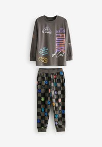 Maglietta grigia a maniche lunghe con testo grafico colorato, abbinata a pantaloni a scacchi neri e grigi con disegni di faccine sorridenti multicolori.