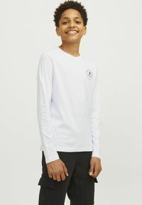 Långärmad vit t-shirt med rund halsringning och en liten tryckt logotyp på bröstet, kombinerad med svarta cargobyxor. Slätt, lättviktigt tyg.