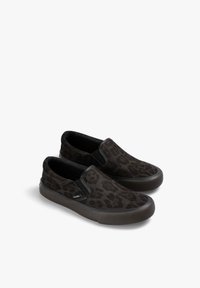Par de zapatillas negras sin cordones con un patrón de leopardo oscuro y suelas de goma, inclinadas a la izquierda sobre un fondo blanco.