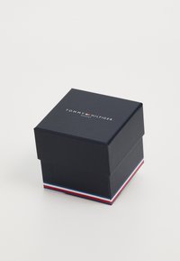 Boîte en carton bleu marine avec fermeture magnétique, ornée d'un logo blanc et d'une bande rayée rouge, blanche et bleue à la base.