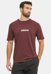 T-shirt corto di colore bordeaux con logo Adidas bianco sul petto, realizzato in tessuto morbido con scollatura rotonda e vestibilità rilassata.