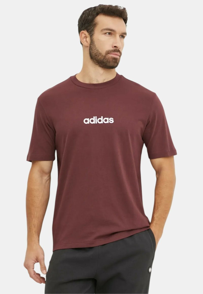 T-shirt corto di colore bordeaux con logo Adidas bianco sul petto, realizzato in tessuto morbido con scollatura rotonda e vestibilità rilassata.