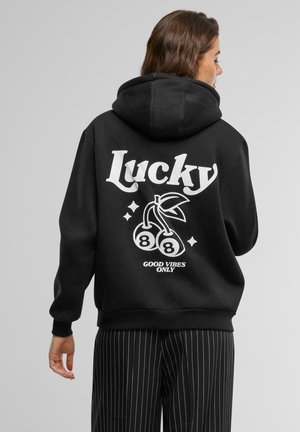 Black hoodie featuring a large white "Lucky" text, cherry graphic, and "Good Vibes Only" text on the back. Soft fabric, relaxed fit.