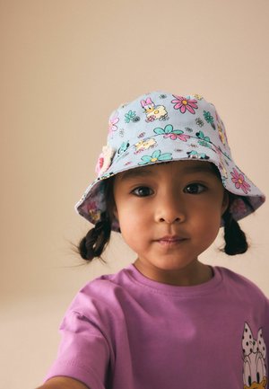 Young girl with braided hair wearing a purple shirt and a pastel floral bucket hat, looking directly at the camera.