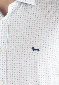 Camicia bianca con bottoni caratterizzata da un motivo geometrico di triangoli e punti azzurri, con un dachshund ricamato in blu navy sul davanti.