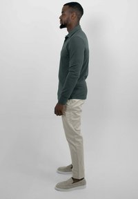 Langermige donkergrijze polo, lichtbeige slim-fit broek en lichtgrijze instap schoenen, zijwaarts bekeken tegen een neutrale achtergrond.