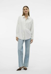 Camicia a righe bianca e azzurro chiaro con maniche lunghe, abbinata a jeans larghi azzurri e scarpe con tacco marroni.