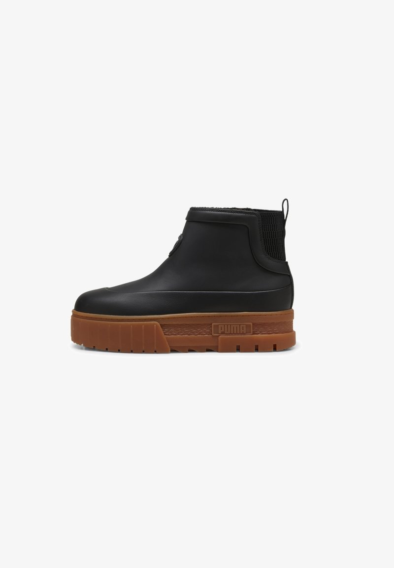 Bottine noire en caoutchouc lisse avec une tige en tricot texturé et une semelle plateforme marron coussinée. Présente un détail logo sur le côté.